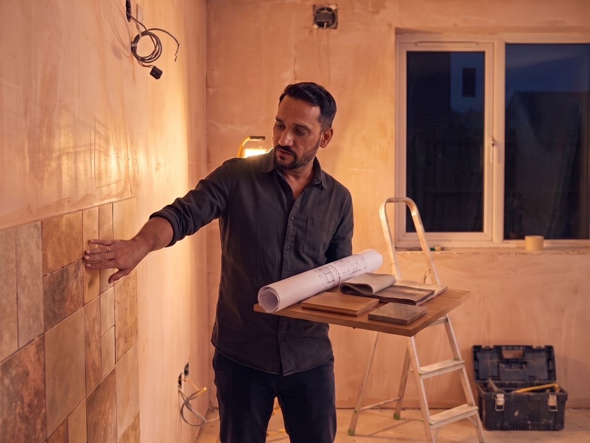 DA Elements designer supervising a fit-out site at night, reviewing architectural drawings and a material sample board.